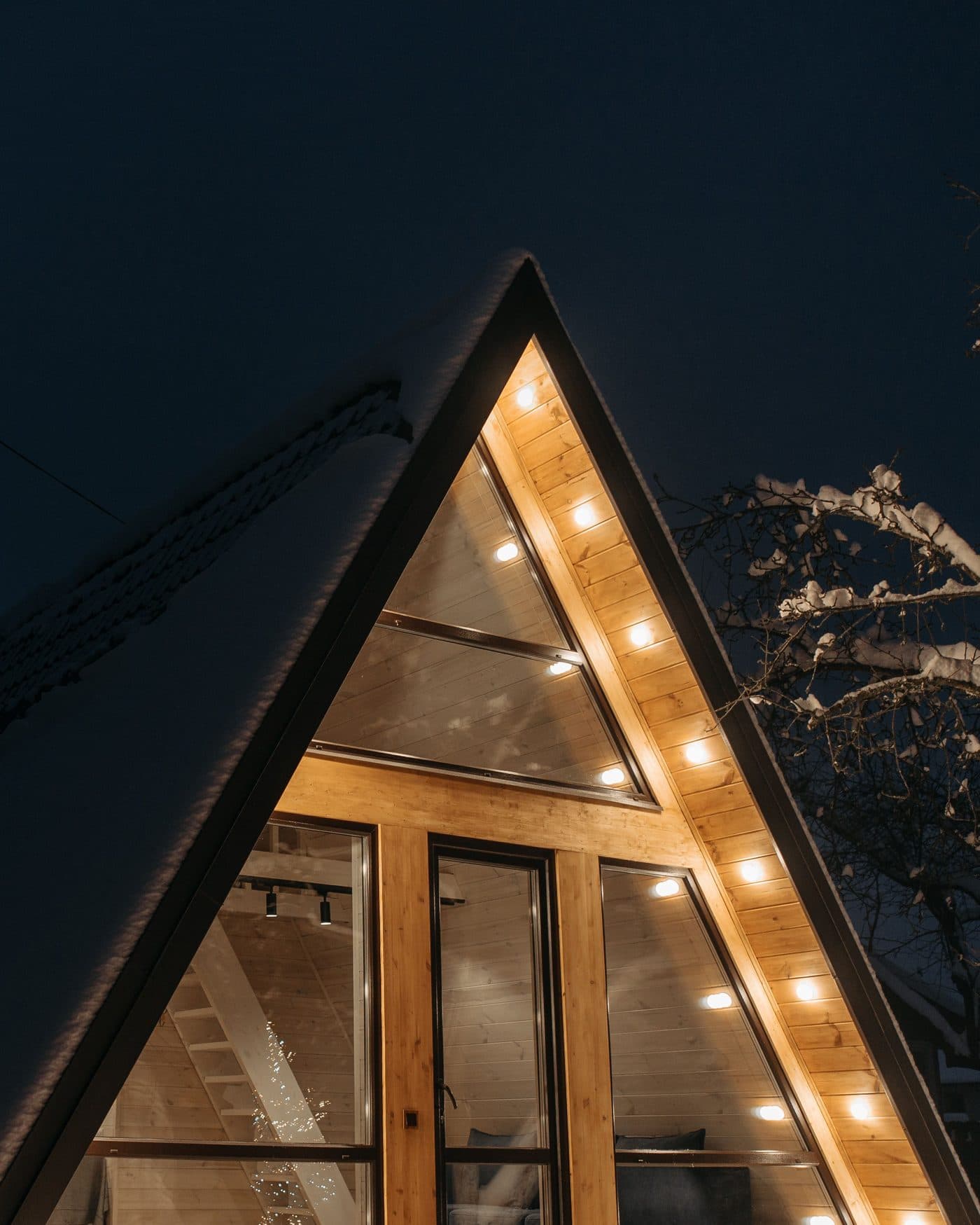 Cabaña de madera iluminada de noche, cubierta de nieve (foto ilustrativa)